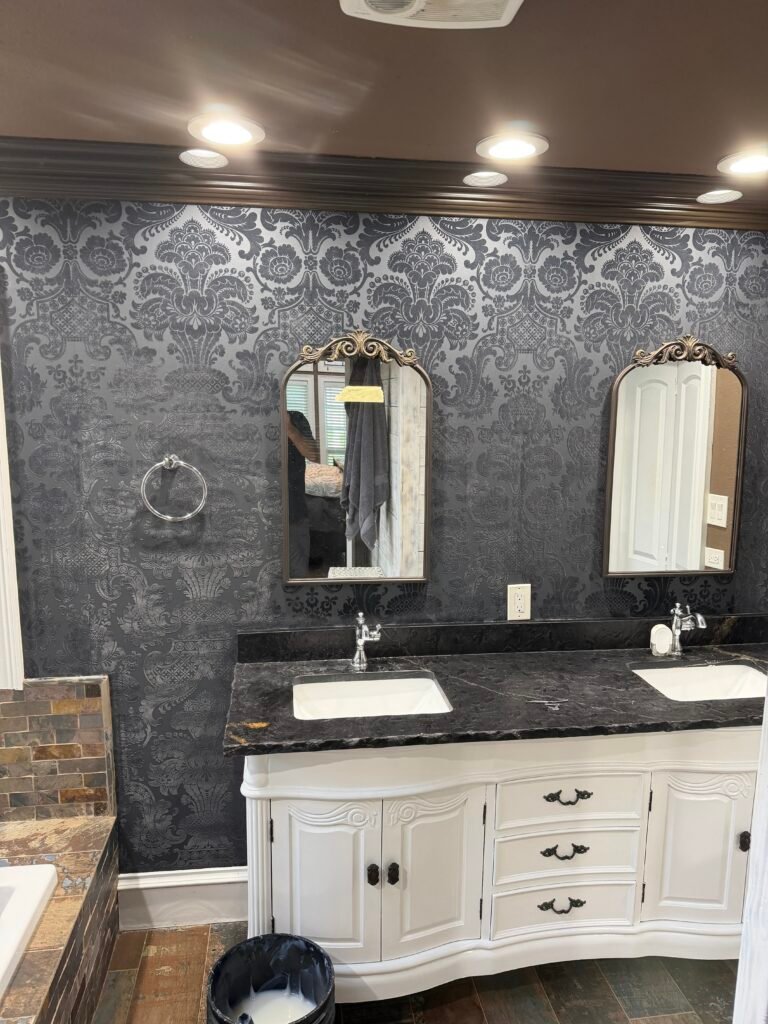 Finished black damask wallpaper accent wall in a residential bathroom with a white double vanity