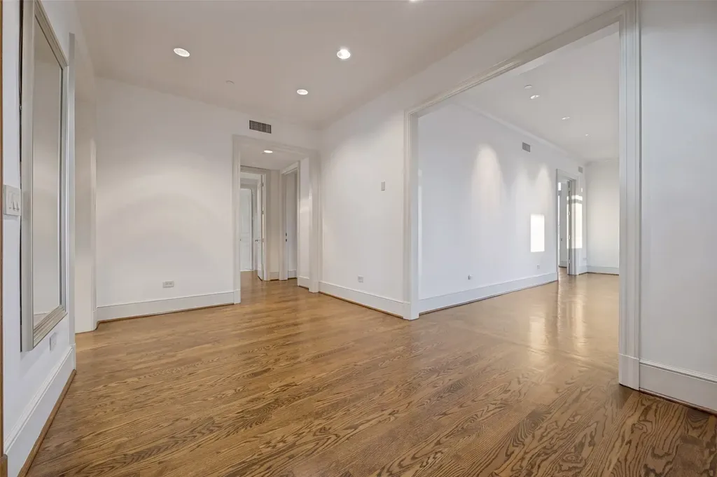 Spacious empty room with freshly painted white walls, white baseboard trim, recessed lighting, and hardwood floors.