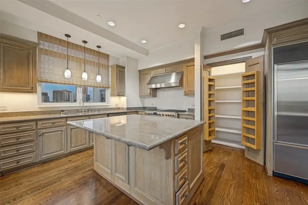 Modern kitchen featuring distressed wood cabinets, large island with polished stone countertop, and open walk-in pantry.