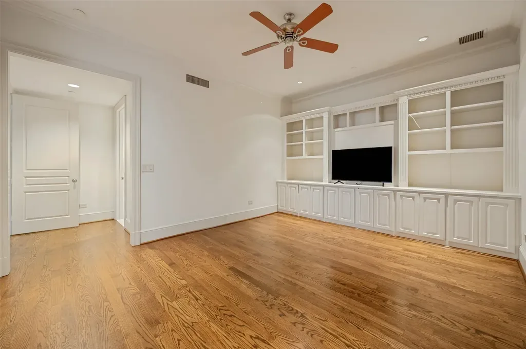Spacious living room featuring hardwood floors, painted white walls, and a large white built-in entertainment center with a TV.