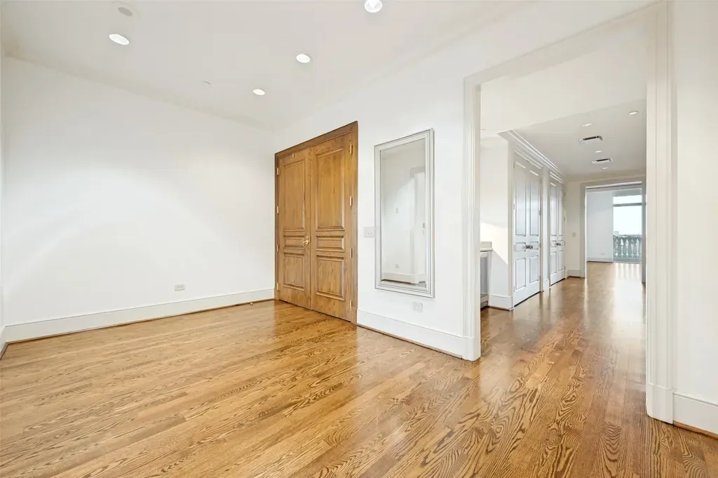 Spacious empty room with freshly painted white walls, wood double doors, hardwood floors, and a hallway view.