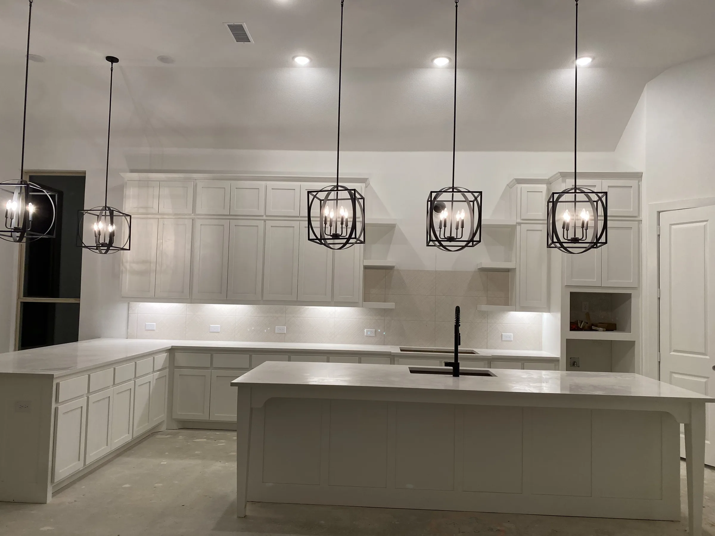 Spacious kitchen featuring painted white cabinets, large center island, and black geometric pendant light fixtures.