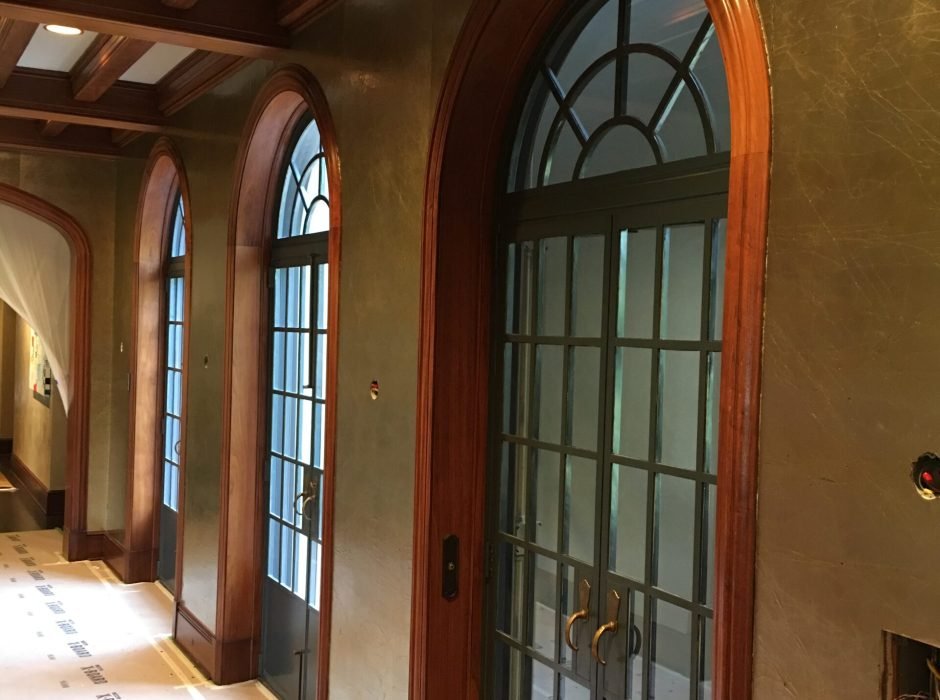 Hallway with textured metallic-finish plaster walls and arched wood-trimmed windows and doors, floor covered in protective paper during a wallcovering installation