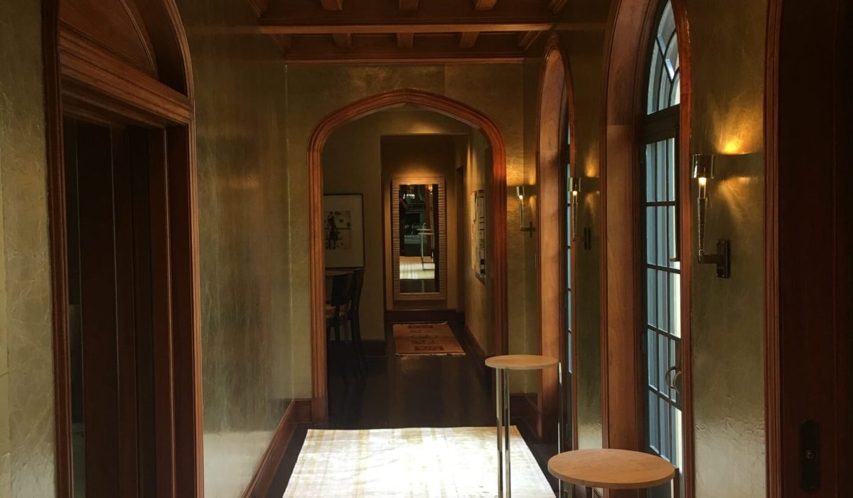 Arched hallway with textured plaster walls, dark wood trim and beamed ceiling, leading to a foyer with a runner rug and mirrored console table