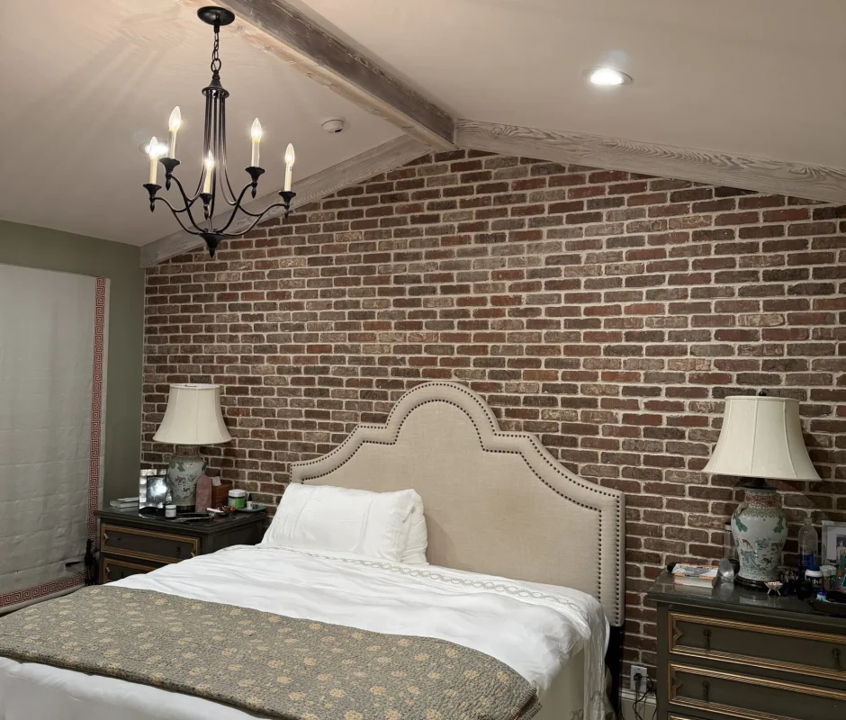Bedroom featuring a brick pattern wallpaper accent wall behind an upholstered bed with nightstands.