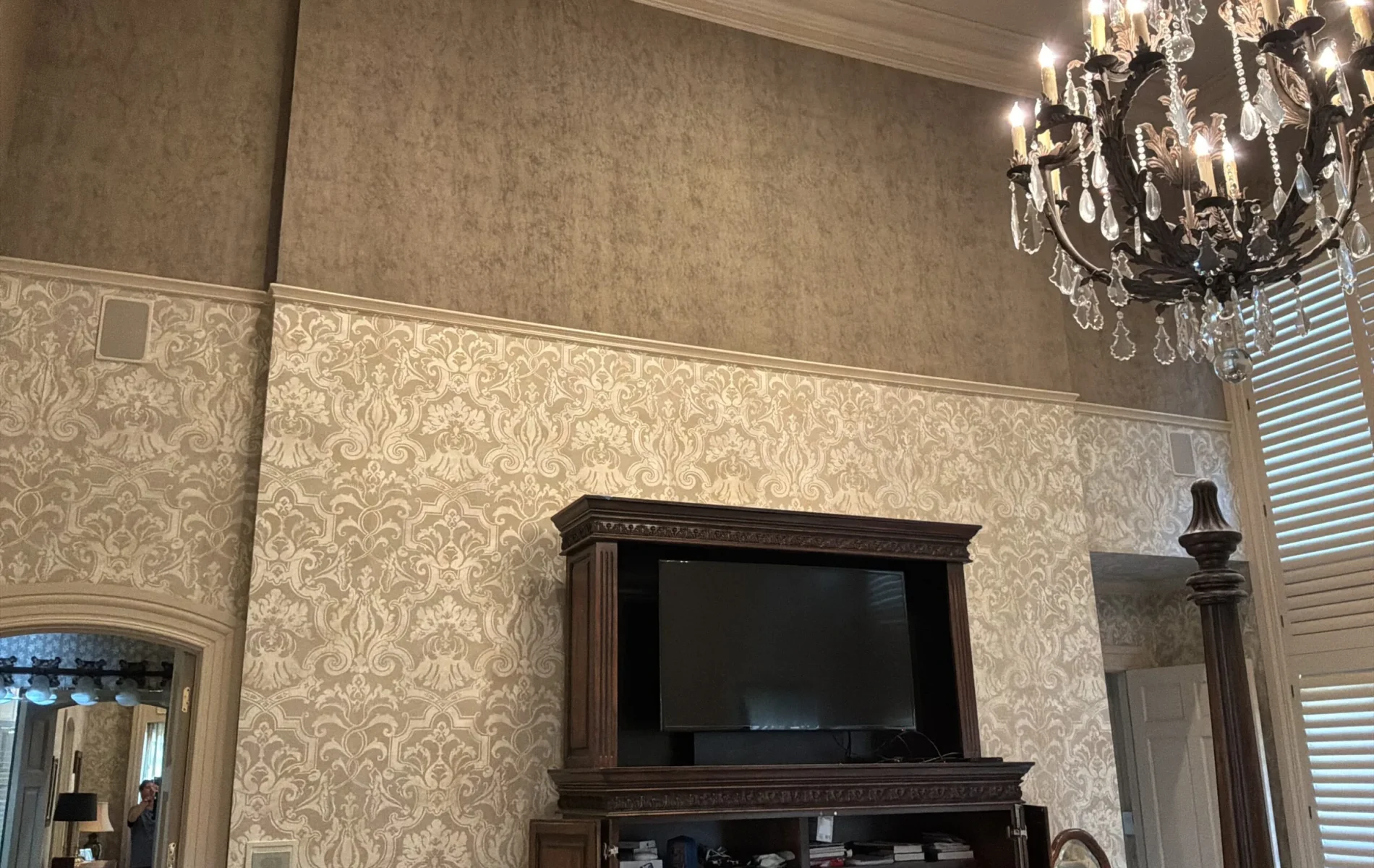 High-ceiling room featuring beige damask wallpaper on lower walls beneath a textured upper wall and ornate chandelier.