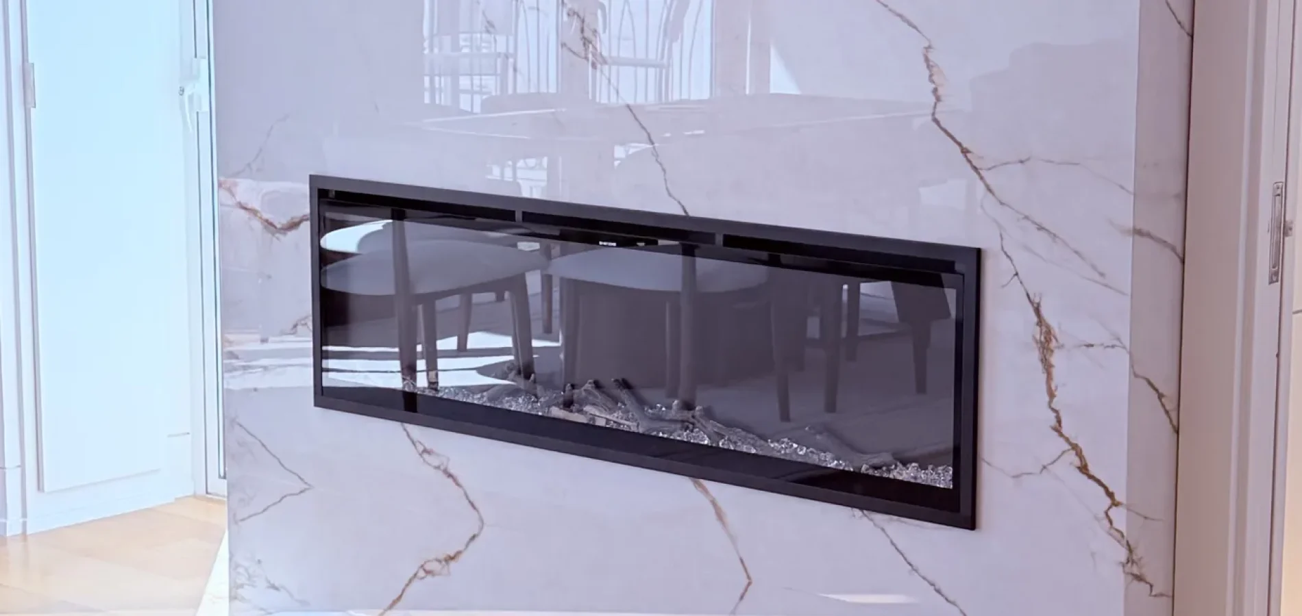 Modern linear fireplace with a glossy white and gold marble pattern surround beneath framed wall art.