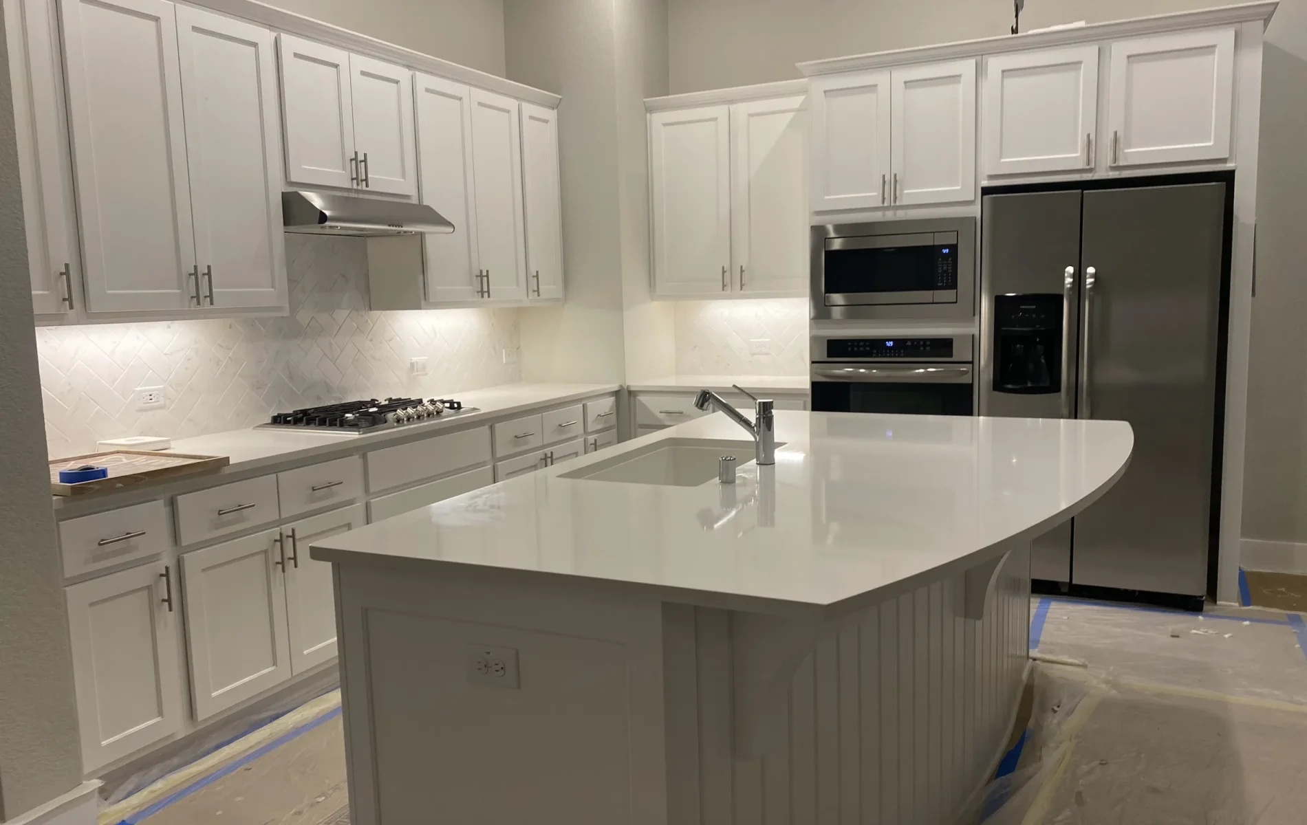 Newly painted white kitchen cabinets and central island with protective plastic sheeting masking the floor.