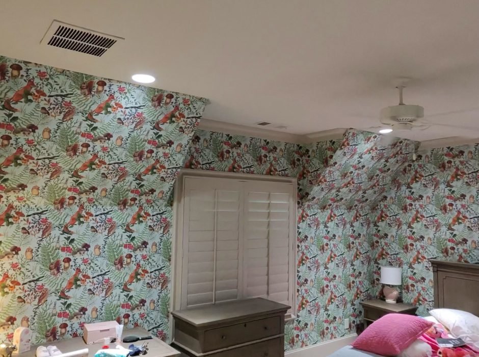 Child's bedroom with sloped ceiling walls papered in a whimsical woodland pattern of birds, foxes, and ferns, with plantation shutters and a wood dresser