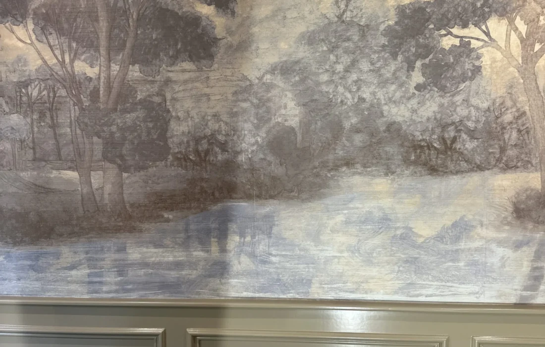 Scenic landscape mural wallpaper installed above painted wainscoting panels.