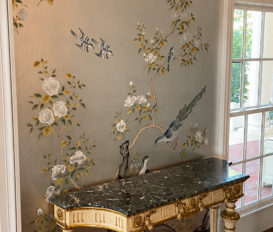 hinoiserie-style wallpaper with hand-painted birds and flowering branches on a soft gray ground, behind a gilded marble-top console table in an entryway